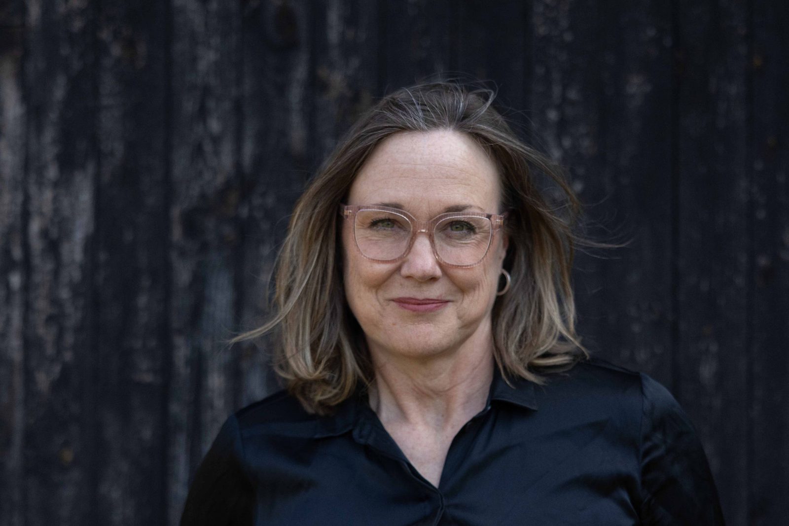 Malin Thorsén mot en mörk träpanel, armarna i kors, tittar rakt in i kameran